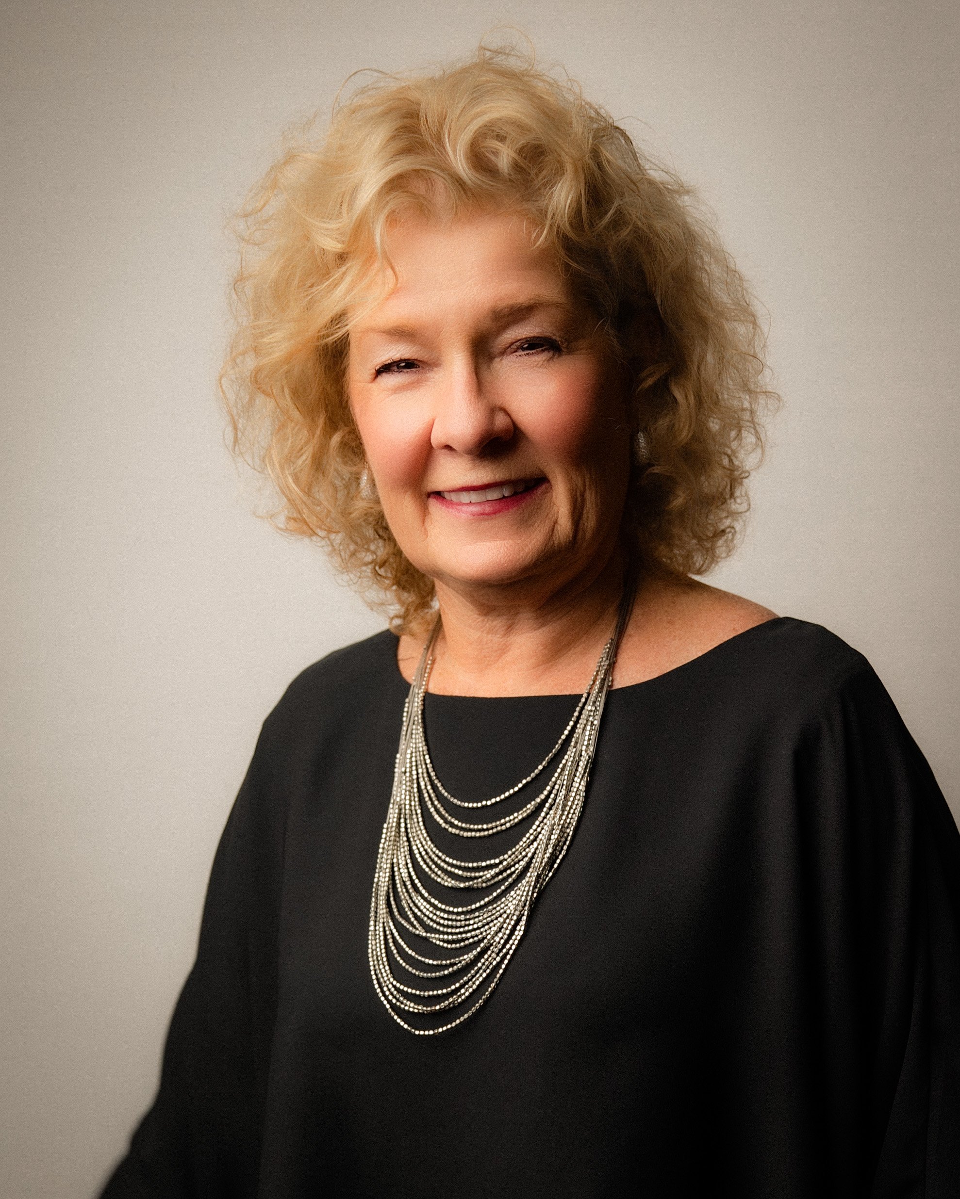 Portrait of Hollie with curly blonde hair and a metallic necklace