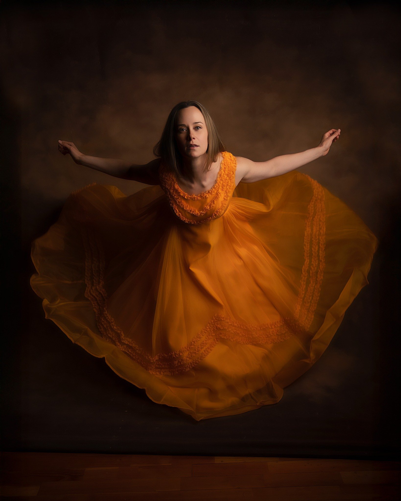 Woman in a flowing orange dress with her arms extended