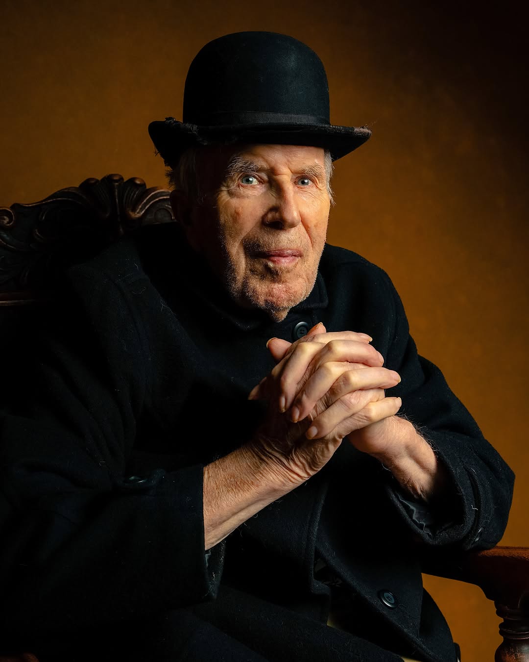 Elderly man in a black bowler hat and dark coat seated in a studio