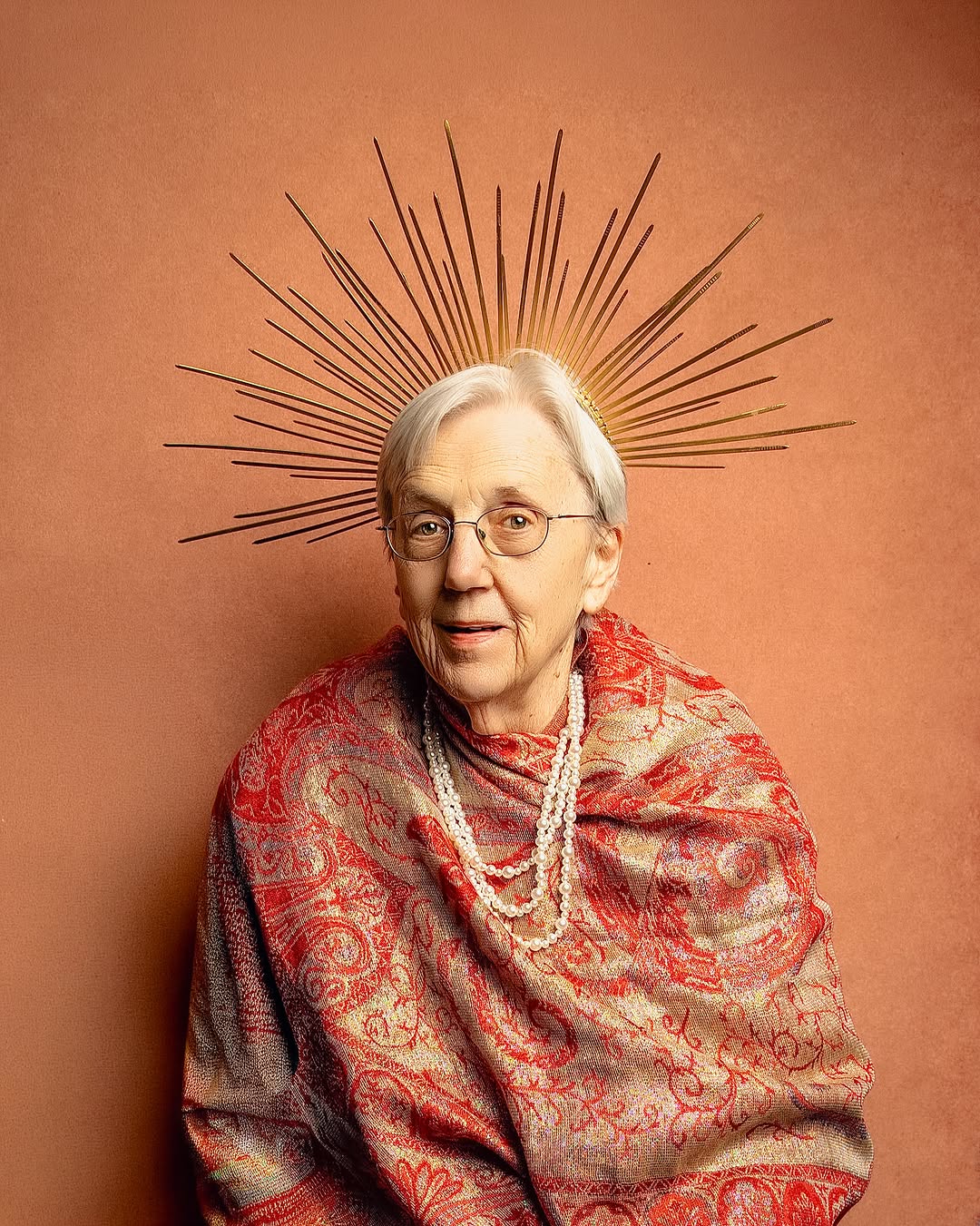Elderly woman with silver hair wearing a golden sunburst headpiece
