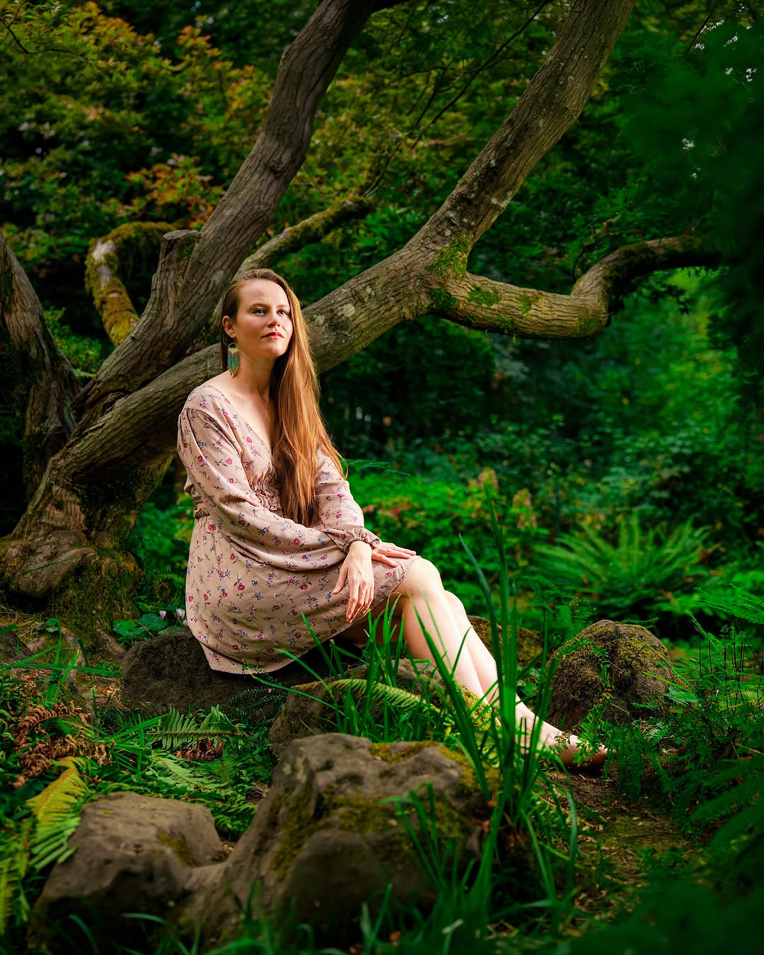 Woman in a floral dress seated among mossy rocks in a lush forest